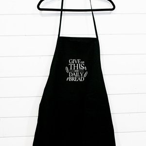 Black apron with white text hanging on a hanger against a white wall.