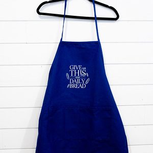 Blue apron with white text hanging on a black hanger against a white wall.